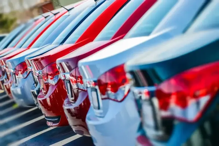 Row of red and white cars parked closely together at a dealership lot, rear ends and taillights in focus