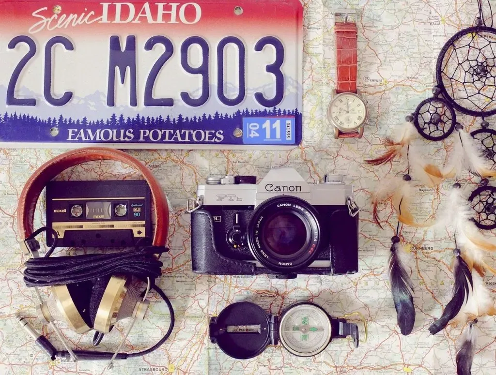 Flat lay on a map with Scenic Idaho license plate, Canon FT camera, headphones, watch, compass, and dreamcatcher
