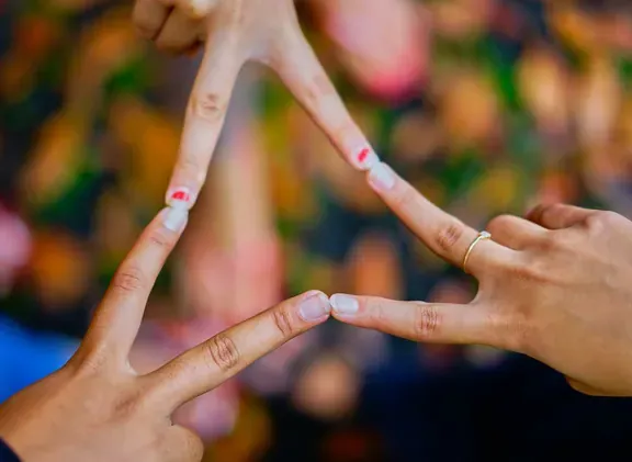 Three hands extending fingers to touch each other forming a connection against a blurred floral background