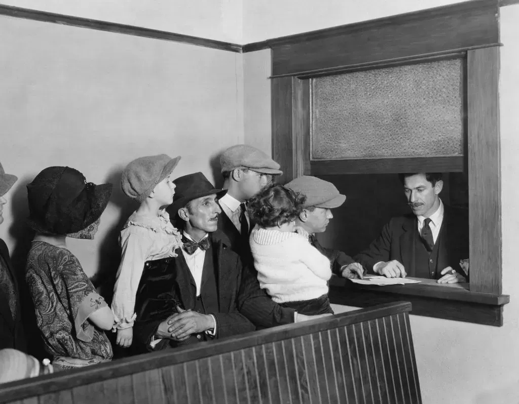 Vintage black and white photo of people in hats crowded at a service window speaking with a clerk