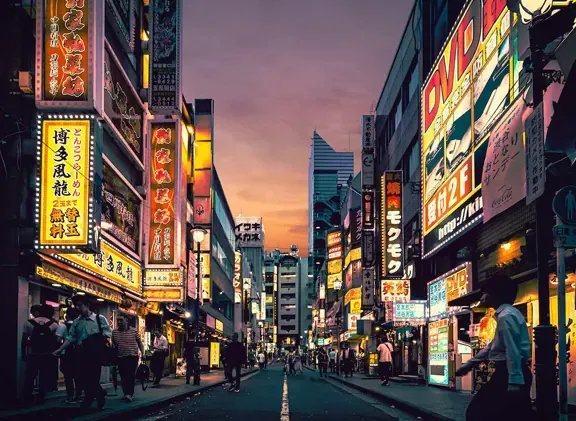 Busy Tokyo street at dusk lined with glowing neon signs in Japanese characters and pedestrians walking along shops
