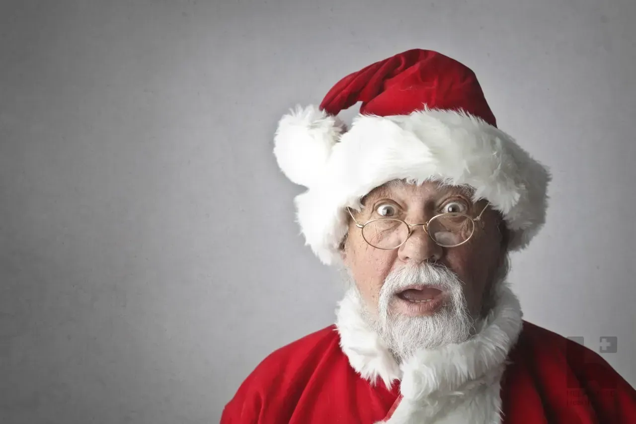 Surprised Santa Claus in red suit and round glasses with wide eyes and open mouth against a gray background
