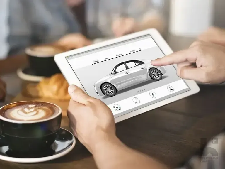Hands holding a tablet displaying a silver car configurator app, beside a latte and croissant on a wooden cafe table