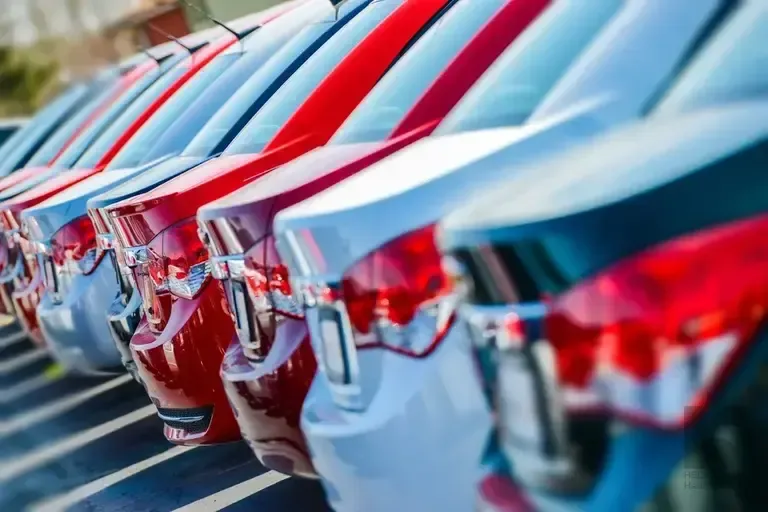 Row of red and white cars parked closely together at a dealership lot, rear ends and taillights in focus